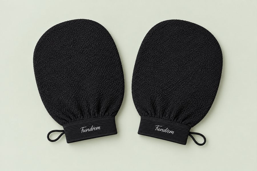 Two black exfoliating mitts on a sage background